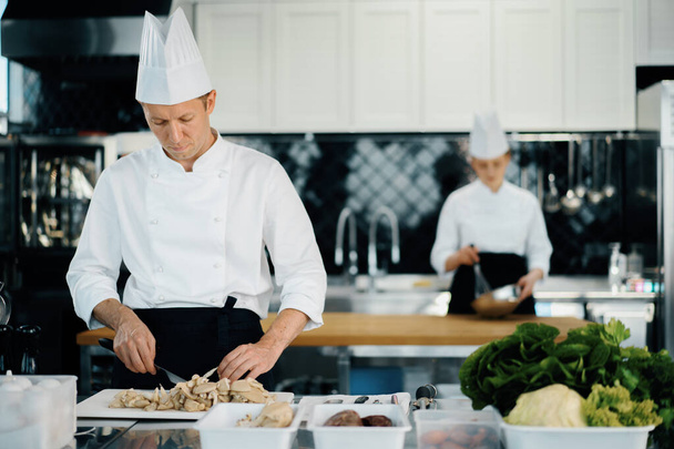 Professional kitchen: two chefs prepare food. The cook cuts mushrooms to prepare delicious dish. - Fotoğraf, Görsel