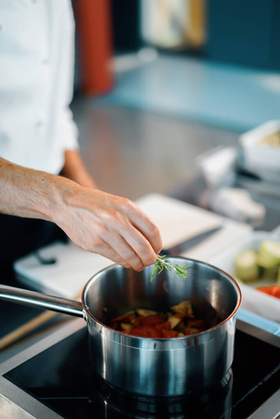 Профессиональная кухня ресторана, крупным планом: шеф-повар бросает зелень в кастрюлю - Фото, изображение