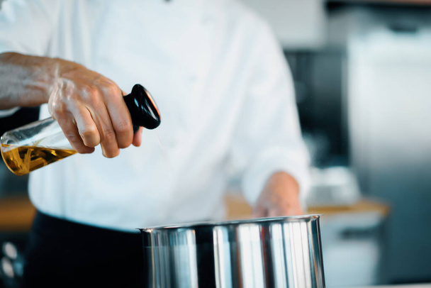 Professional restaurant kitchen, close-up: the chef splashes oil on pan - Foto, afbeelding