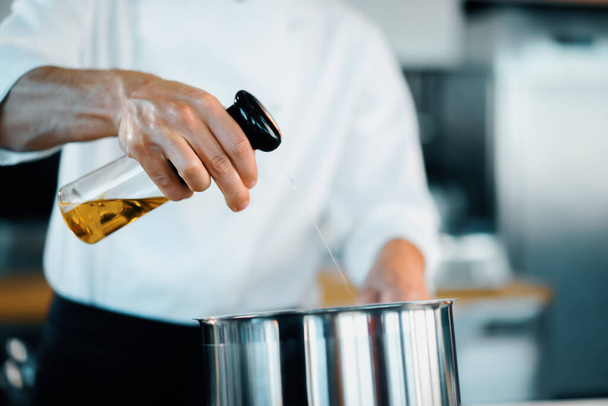 Professional restaurant kitchen, close-up: the chef splashes oil on pan - 写真・画像