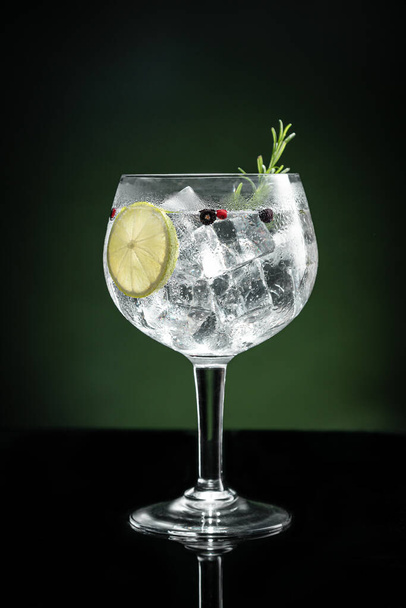 Cold glass of gin tonic with ice on dark green background with copy space. Vertical format. - Fotoğraf, Görsel
