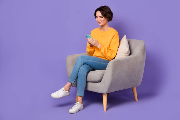 Portrait of attractive cheerful trendy girl sitting in chair using gadget 5g post isolated over violet lilac color background. - Photo, image
