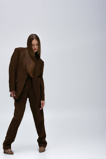 full length of brunette teenage model in brown high-quality suit posing on grey - Foto, Imagem