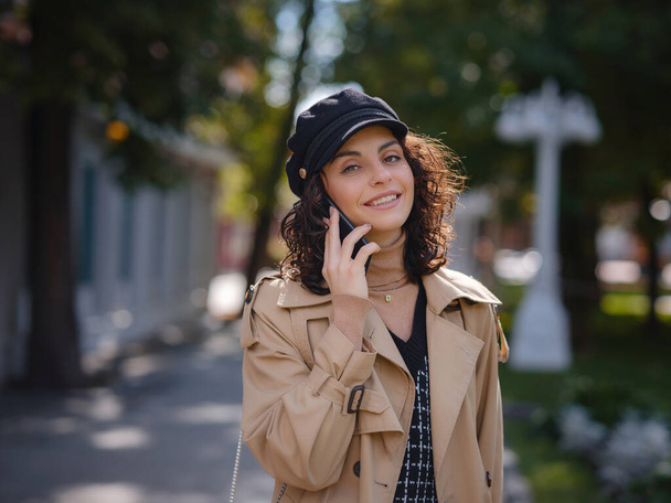 Outdoors lifestyle fashion portrait of pretty young lady talking on smartphone. Young hispanic or Armenian woman wearing elegant style standing at Moscow city. - 写真・画像