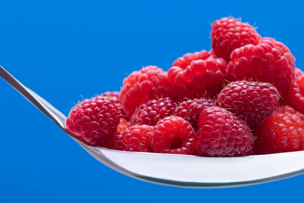 Fresh organic raspberry on a metal spoon on blue background.  - Foto, imagen