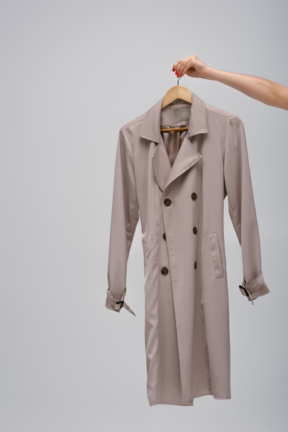 cropped view of woman holding recyclable trench coat on hanger isolated on grey - Fotó, kép