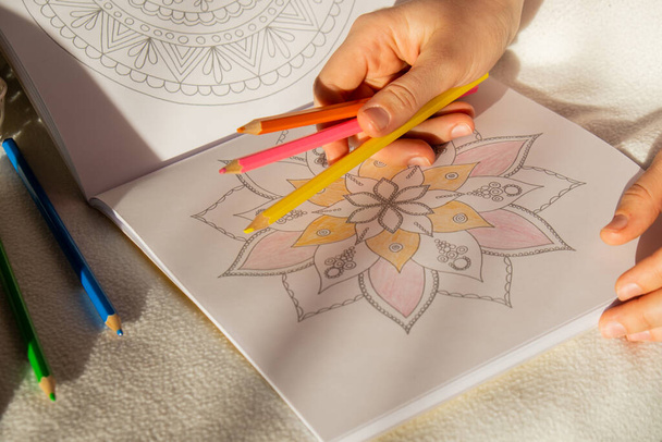 Frau färbt Antistress-Seite aus. Weibliche Hand bemalt Mandala. Frauen malen Mandalas, um Stress zu bekämpfen. Entspannendes Hobby psychische Wohlbefinden und Kunsttherapie. Frau malt Skizze, meditativen Prozess der - Foto, Bild