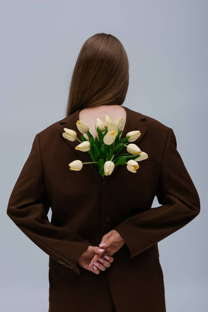 back view of brunette model in brown blazer with tulips isolated on grey - Fotografie, Obrázek