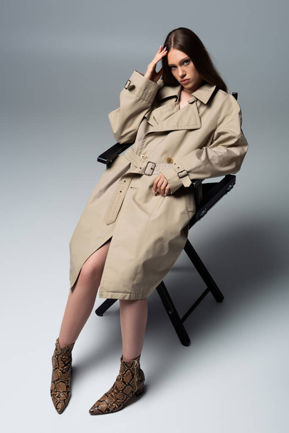 full length of model in stylish trench coat posing on chair of grey - Foto, immagini