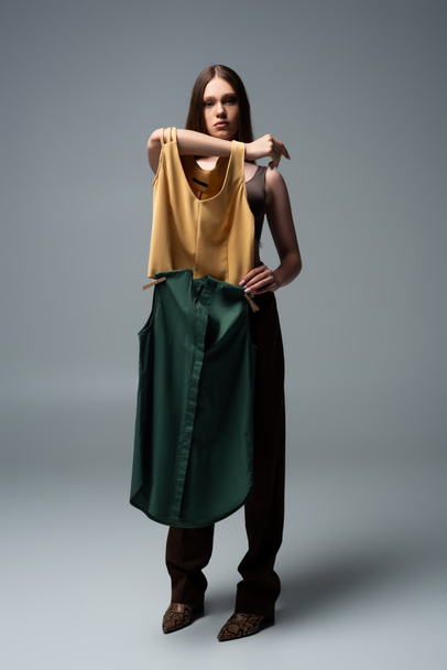 full length of brunette model holding clothing with clothespins on grey  - Valokuva, kuva