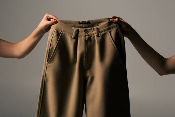 καλλιεργούμενη άποψη των γυναικών που κατέχουν ανακυκλώσιμα μπεζ παντελόνια που απομονώνονται σε γκρι - Φωτογραφία, εικόνα