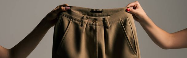 cropped view of women holding recyclable beige trousers isolated on grey, banner - 写真・画像
