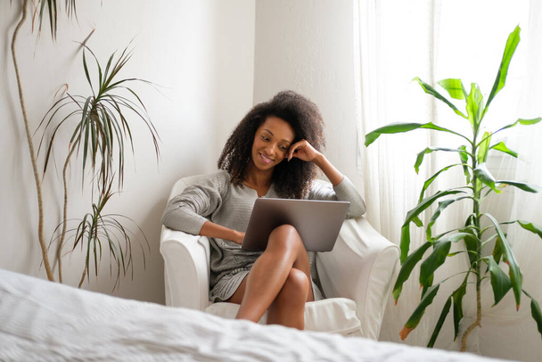 Relaxed casual afro hairstyle woman using laptop at home in her bedroom. - Foto, Imagen