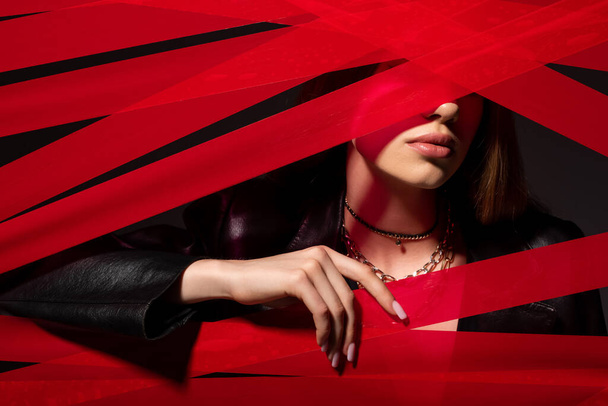 young model touching red strips from duct tape isolated on black, recycle fashion concept - 写真・画像