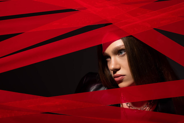 teenage model looking away through red strips from duct tape isolated on black, recycle fashion concept - Φωτογραφία, εικόνα