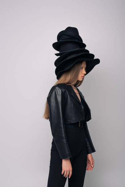 side view of brunette model in leather jacket and different black hats on head isolated on grey - Foto, Bild