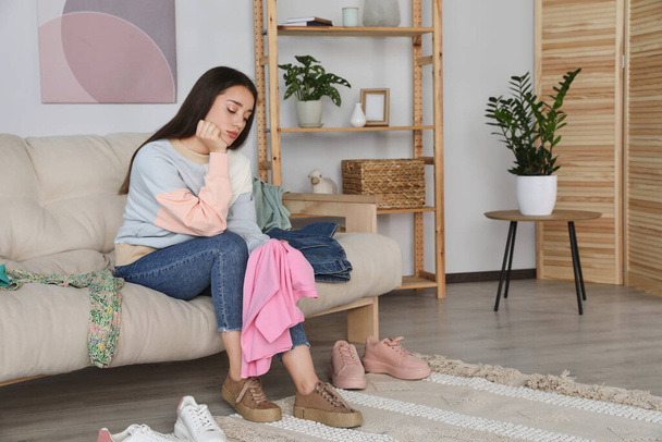 Upset young woman with clothes on sofa at home, space for text - Photo, Image