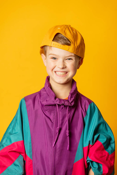 Κομψό παιδί αγόρι στη δεκαετία του '80 σπορ κοστούμι και καπέλο σε κίτρινο φόντο - Φωτογραφία, εικόνα