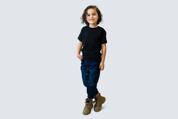 Full length of an adorable boy wearing jeans and a black mockup black t-shirt while smiling in front of a white background - Fotó, kép
