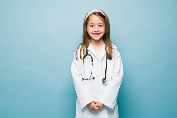 Caucasian girl with a medical aspiring career wearing a lab coat and dressed as a doctor against a blue background with copy space - Foto, Bild