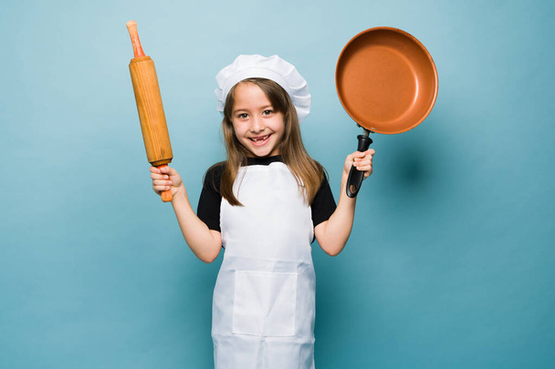 Cheerful caucasian little girl smiling with a chef's hat playing with pots and pans while playing to cook  - Fotó, kép