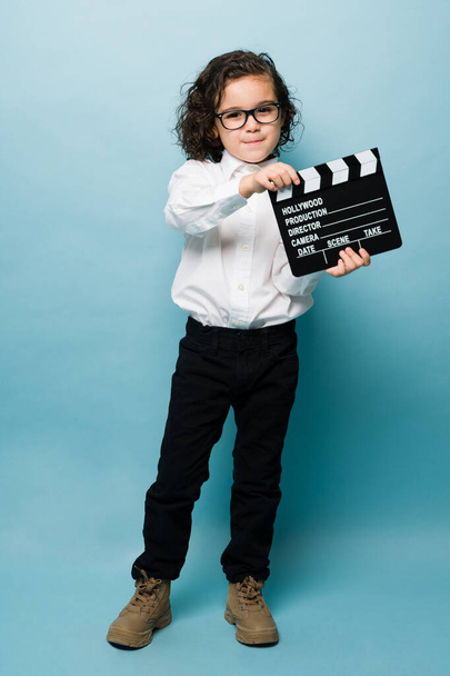 Full length of an adorable little boy using a clapperboard and dreaming to work as a movie director or in entertainment - Foto, Imagem