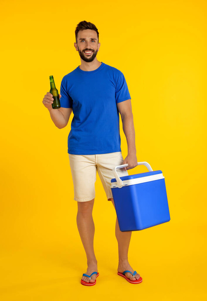 Happy man with cool box and bottle of beer on yellow background - Foto, afbeelding