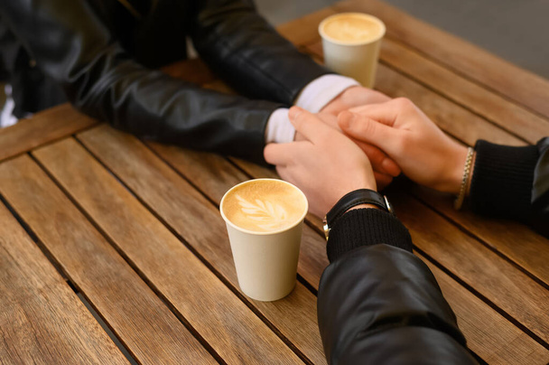 Preciosa pareja con café tomados de la mano en la mesa de madera al aire libre, primer plano. Fecha romántica - Foto, Imagen