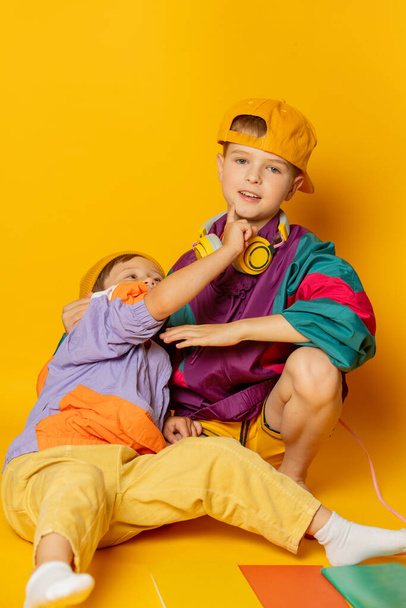 Two kids in stylish vintage 80s clothes have a fun on yellow background - Fotoğraf, Görsel