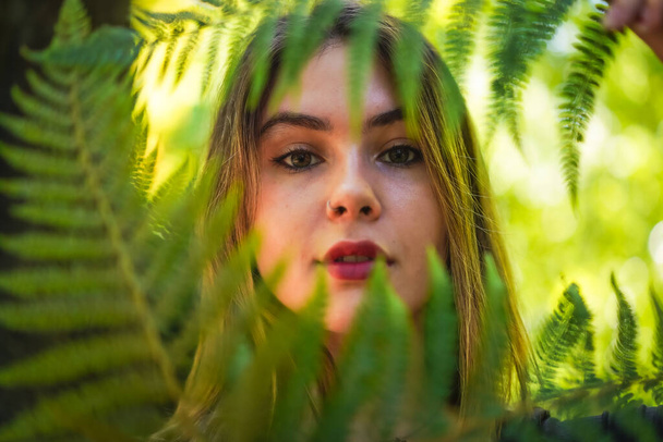 Portrait of a young woman in nature in a natural park with some fern leaves - Фото, зображення