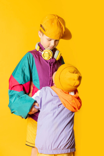 Two kids in stylish vintage 80s clothes have a fun on yellow background  - Fotoğraf, Görsel