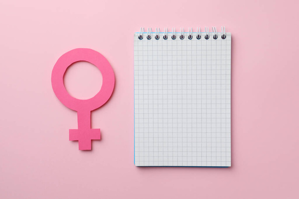 Female gender sign as women's health symbol and notebook on pink background, flat lay. Space for text - Фото, изображение