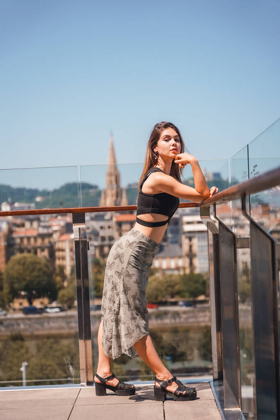 Posing of a young woman on the terrace of a hotel looking at the city from above, glass railing - 写真・画像