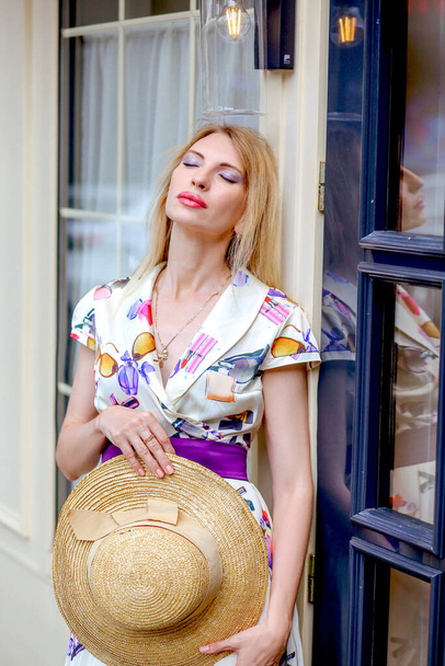 Tired blond model girl closing her eyes in a light dress near a beige wooden door. Summer. City Style. Fashion and beauty. - Фото, зображення