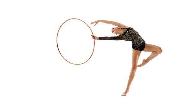 Portrait of young girl, female rhytmic gymnast training with hoop isolated over white studio background. Flexibility. Concept of action, motion, sport life, motivation, competition. Copyspace for ad - Zdjęcie, obraz