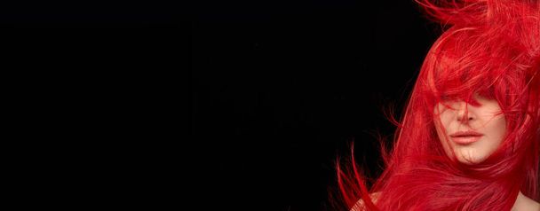 Red haired woman with a beautiful and healthy long red hair. Flying hair isolated on black background with copy space - 写真・画像