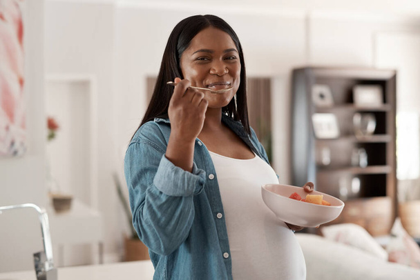 Mommy and baby both need to eat healthy too. Portrait of a pregnant woman eating a bowl of fruit at home - Fotoğraf, Görsel