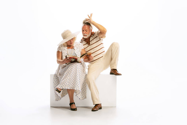 Flirt. Emotional senior man and woman in her 60s in vintage attire sitting together isolated on white background. Concept of relationship psychology, age, retro fashion, old generation - Photo, Image