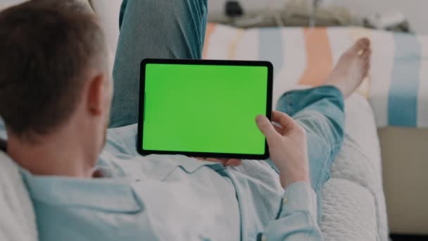 leisure time at home man lying on a couch wearing casual shirt holding digital tablet horizontally scrolling on green screen - Materiał filmowy, wideo