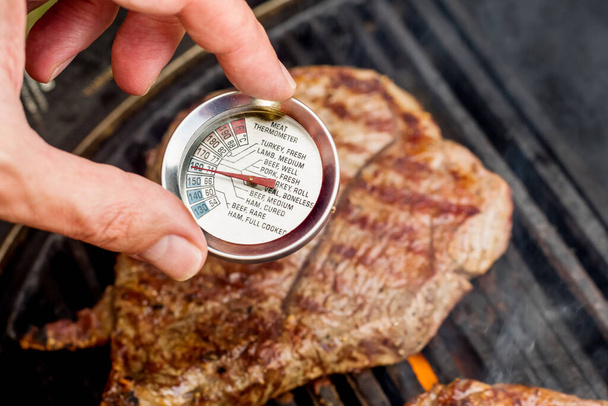 Beef blade steak grilling on barbecue grill plate with meat thermometer. Backyard BBQ grill cooking meat. - Photo, image