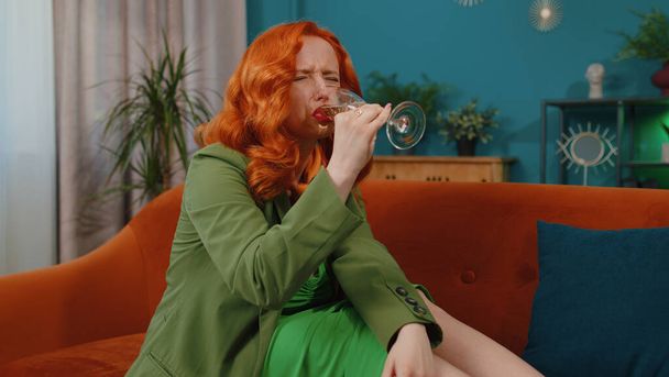 Sad young redhead woman sitting at home looks pensive of unrequited love, suffers from unfair situation, drinking champagne. Girl problems, break up, depressed feeling bad annoyed, burnout, bankruptcy - Foto, Bild