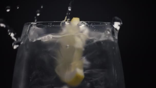 Citrus valwater liet glas van dichtbij vallen. Koud water met ijsblokjes en citroenschijfje in macro. Drank klaarmaken in doorzichtig wijnglas met belletjes. Concept voor het maken en mixen van cocktails - Video