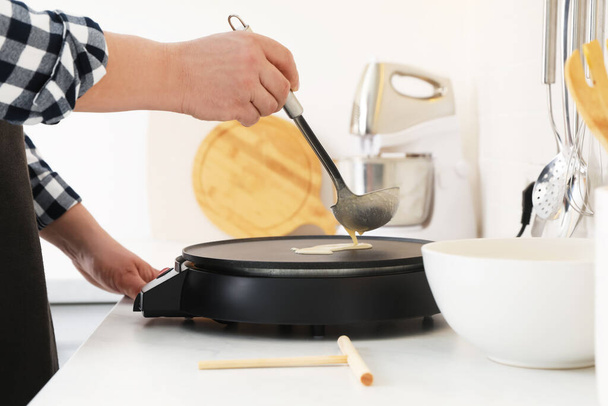 Man cooking delicious crepe on electric pancake maker in kitchen, closeup - Fotografie, Obrázek