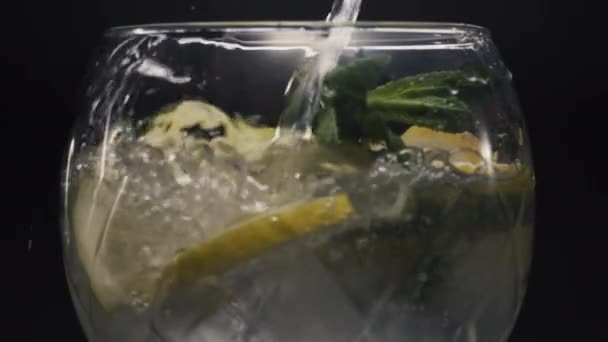 Cocktail de hortelã gelada com limão. Vinho cheio de ervas geladas e limas enchendo com água doce em macro. Cocktail de limonada espumante vista de fundo preto. Preparação do conceito de bebida fresca - Filmagem, Vídeo