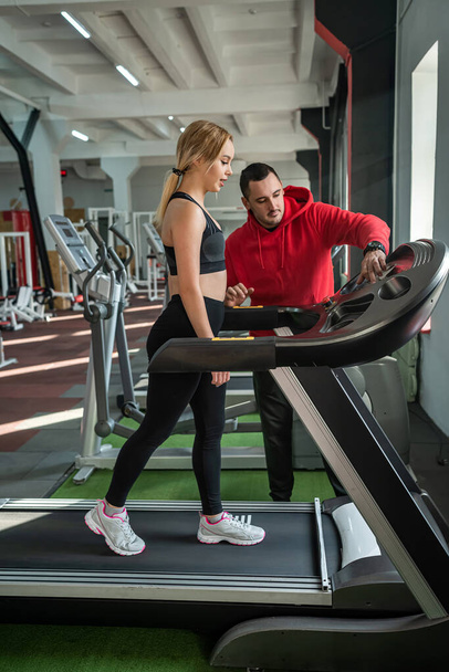 Fit female client running on treadmill with her personal trainer in a sport centre. sportive lifestyle - Фото, изображение