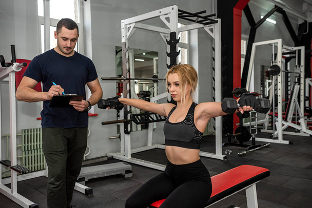 männliche Trainer helfen ihrer Kundin, im Fitnessstudio mit Hantelgewichten zu arbeiten. Aktiver Lebensstil - Foto, Bild