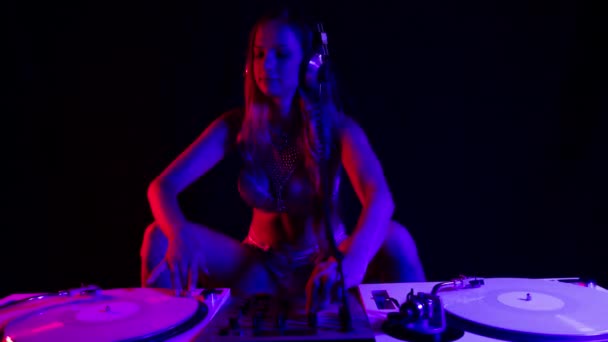 Beautiful female dj playing with turntables with blue and red contrasting lights - Felvétel, videó