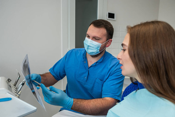 Ένας επαγγελματίας οδοντίατρος δείχνει στον ασθενή φωτογραφίες από το σαγόνι και τα δόντια του. Η έννοια των εικόνων της γνάθου και των δοντιών στον οδοντίατρο - Φωτογραφία, εικόνα