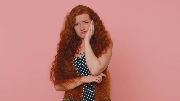 Dental problems. Young redhead woman touching cheek, closing eyes with expression of terrible suffer from painful toothache, sensitive teeth, cavities. Ginger girl with freckles on pink background - Foto, Bild