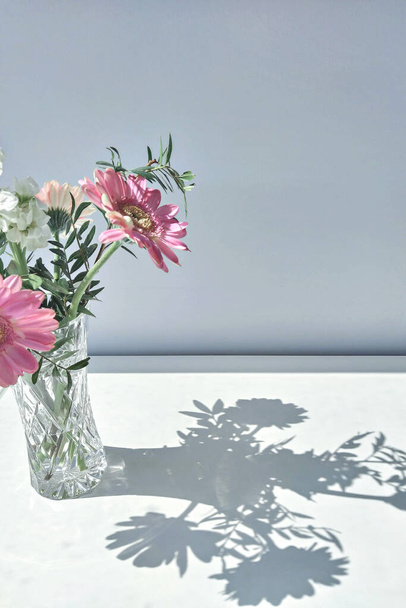 Three pink gerber flowers in small vase by window, home decor spring background with flowers, copy space - 写真・画像